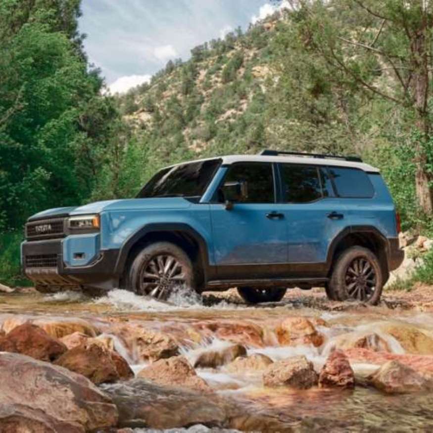 Toyota Land Cruiser crossing rugged terrain in a scenic forest stream.