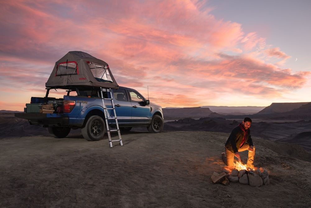 Ford F-150 with aftermarket accessories, rooftop tent, and camping gear at sunset.