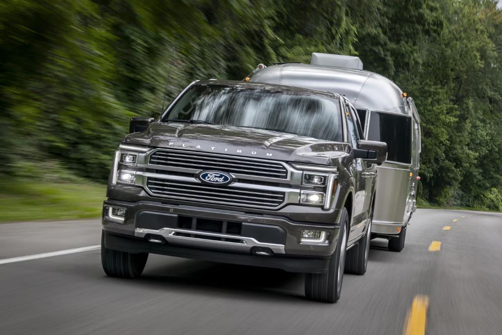 Ford F-150 Platinum towing a trailer on a wooded road.