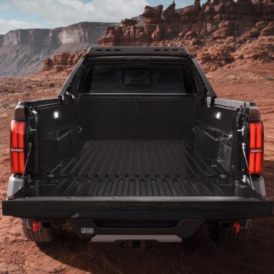 A black Toyota Tacoma truck bed with a huge tailgate open, set against a red rocky desert landscape.